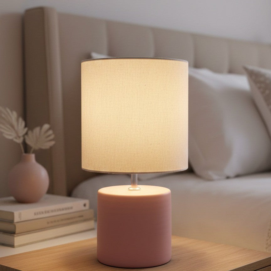 Abajur de cerâmica cilindro rosa queimado aceso no criado-mudo - Vittara Decor