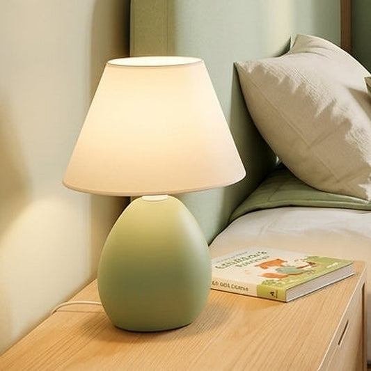 Abajur de cerâmica elipse pistache aceso na cabeceira da cama - Vittara Decor