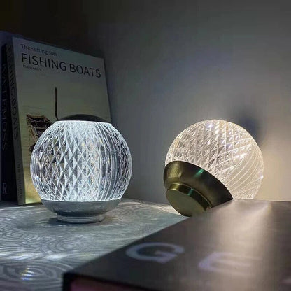 Dois abajures de cristal acesos sobre prateleira ao lado de livros - Vittara Decor