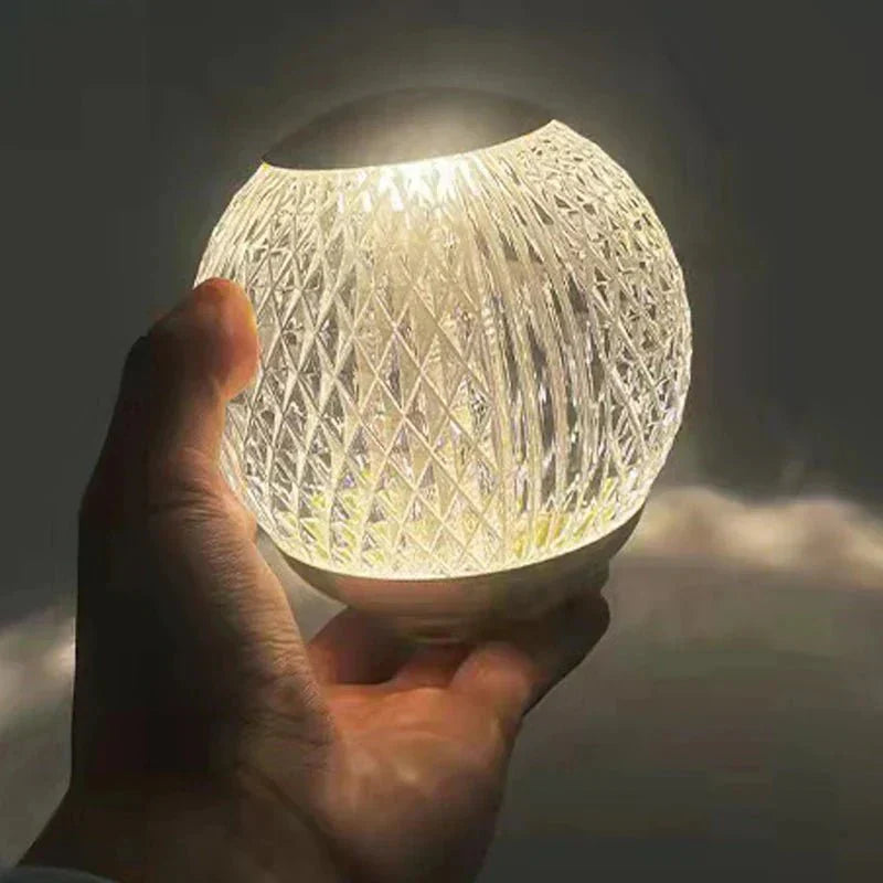 Abajur de cristal esfera segurado na mao, com luz quente brilhando pelas facetas - Vittara Decor