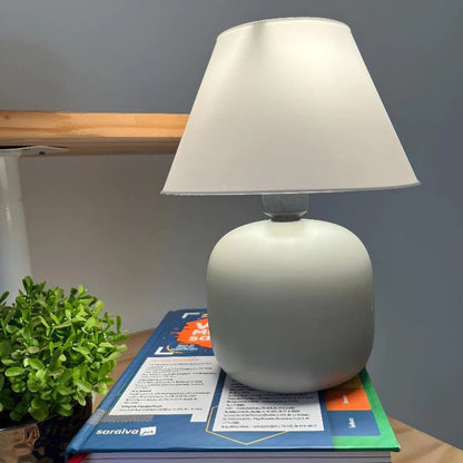 Abajur de Mesa em Cerâmica e Tecido Bivolt na cor Off White sobre livros em escrivaninha - Vittara Decor