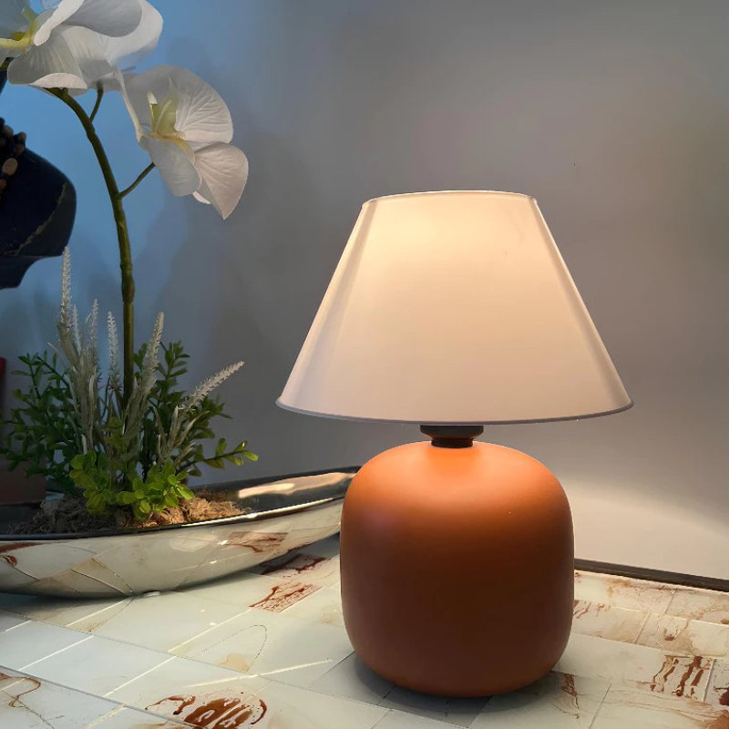 Abajur de Mesa em Cerâmica e Tecido Bivolt na cor Terracota sobre superfície com orquídea branca - Vittara Decor