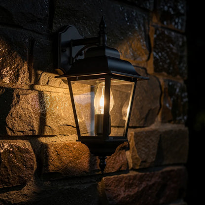 Arandela colonial preta a noite em parede de pedra rustica com brilho ambar — Vittara Decor
