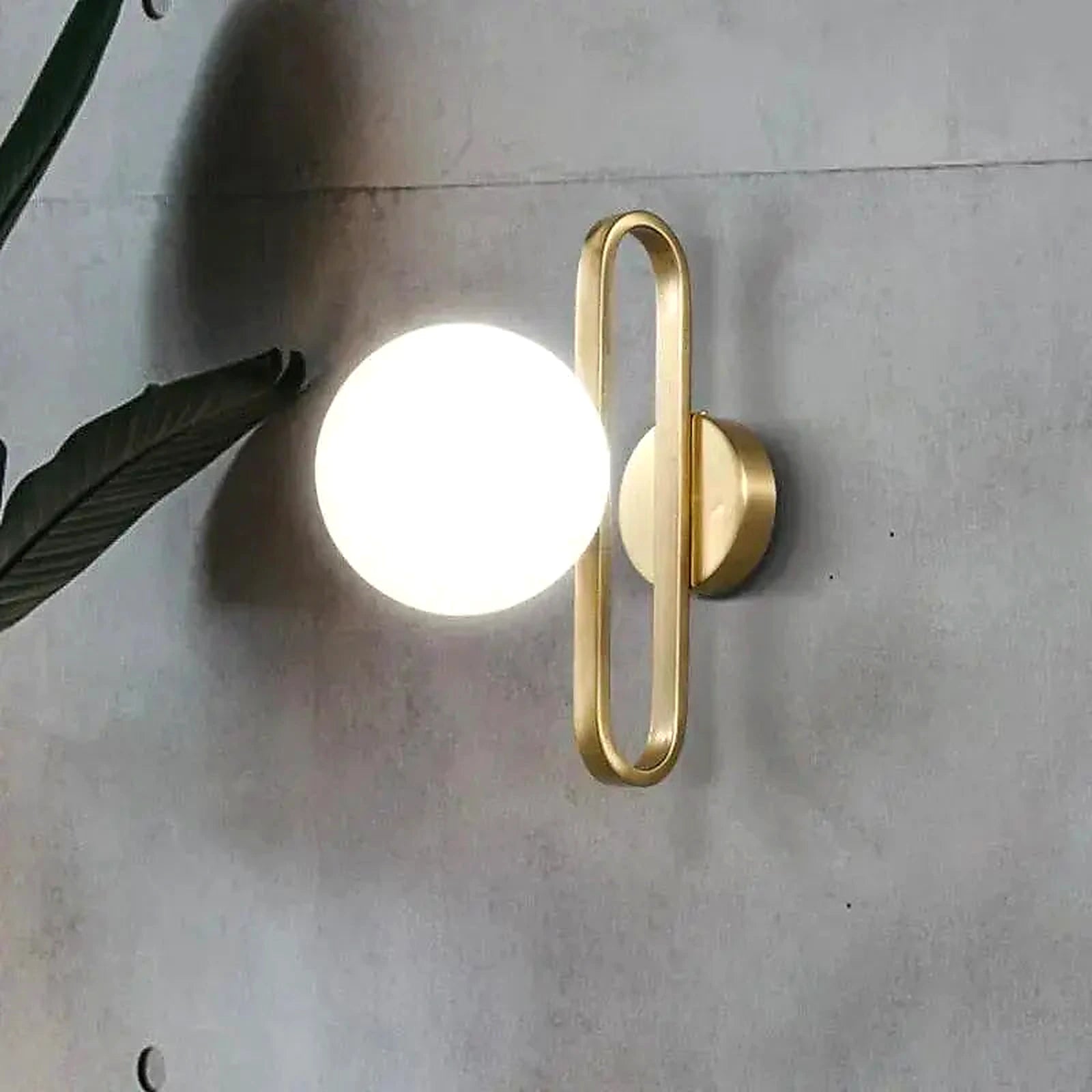Arandela de Parede Dourada LED G9 em parede de concreto com folhagem decorativa