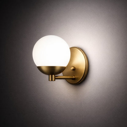 Arandela de parede dourada acesa em ambiente escuro, com luz espalhada pela parede - Vittara Decor