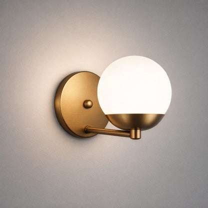 Arandela dourada acesa com luz quente em parede cinza, globo opalino iluminado - Vittara Decor