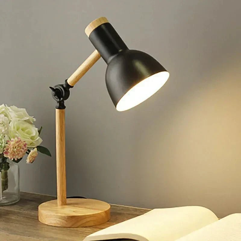 Luminária de mesa articulada preta acesa sobre mesa de madeira - Vittara Decor