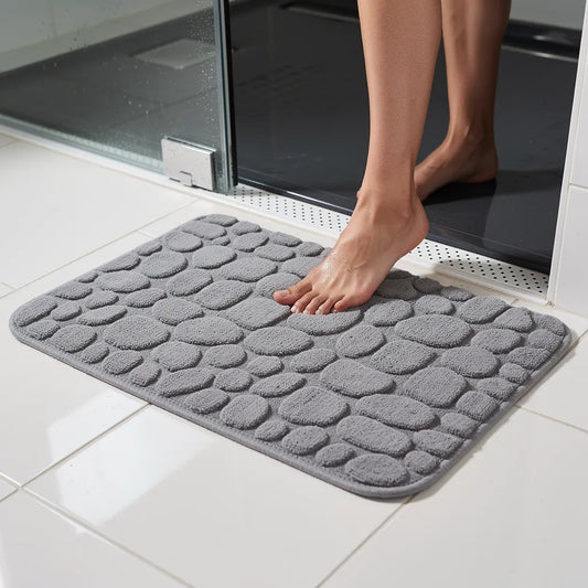 Tapete antiderrapante absorvente cinza em algodão com padrão seixos na saída do box com pé pisando na superfície macia - Vittara Decor