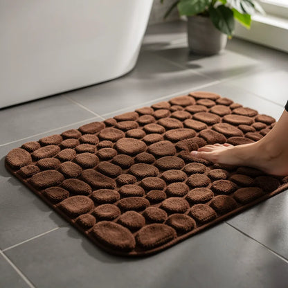 Tapete antiderrapante absorvente marrom em algodão com padrão pedras em relevo posicionado no piso de banheiro com pé descalço - Vittara Decor