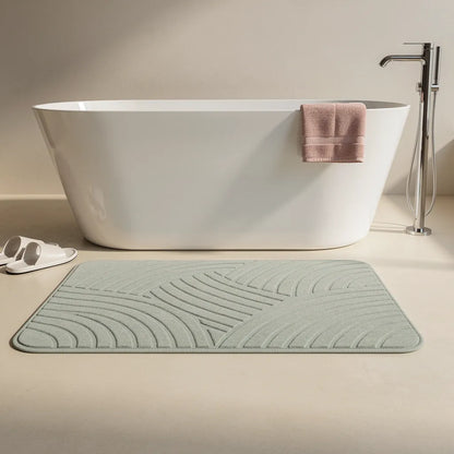 Tapete de diatomita cinza claro posicionado em frente a banheira freestanding em banheiro de estilo spa com toalha e chinelos - Vittara Decor