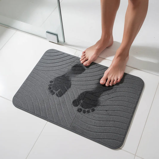 Tapete de diatomita cinza escuro com pés molhados saindo do chuveiro mostrando absorção imediata da água na superfície - Vittara Decor
