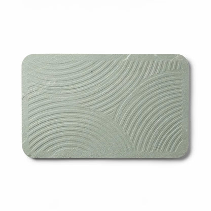 Tapete de diatomita cinza claro em fundo branco mostrando padrão geométrico ondulado em relevo e cantos arredondados 60x40cm - Vittara Decor
